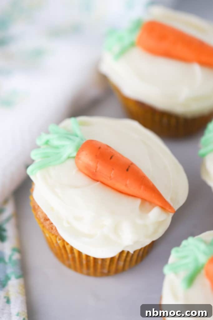 Carrot cake cupcakes topped with frosting and mini carrot candy decorations.