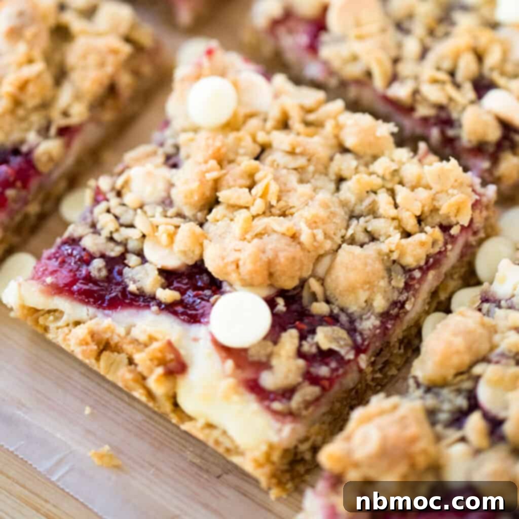 Close-up of freshly baked White Chocolate Raspberry Cheesecake Bars cut into perfect squares, showcasing the oatmeal crumble, creamy white chocolate, and vibrant raspberry swirl.
