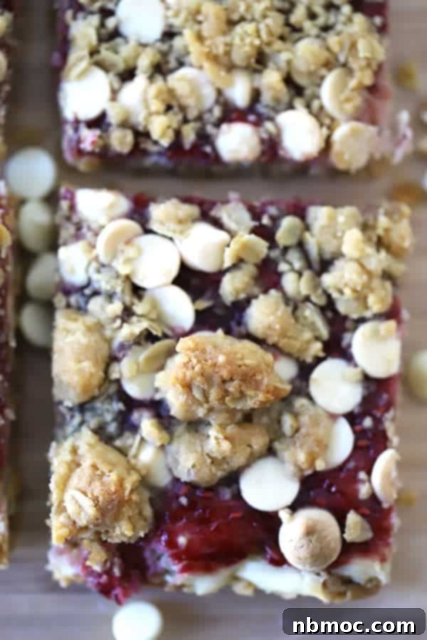 A close-up view of a hand holding a perfectly cut square of Oatmeal Raspberry White Chocolate Blondie, ready to be eaten.