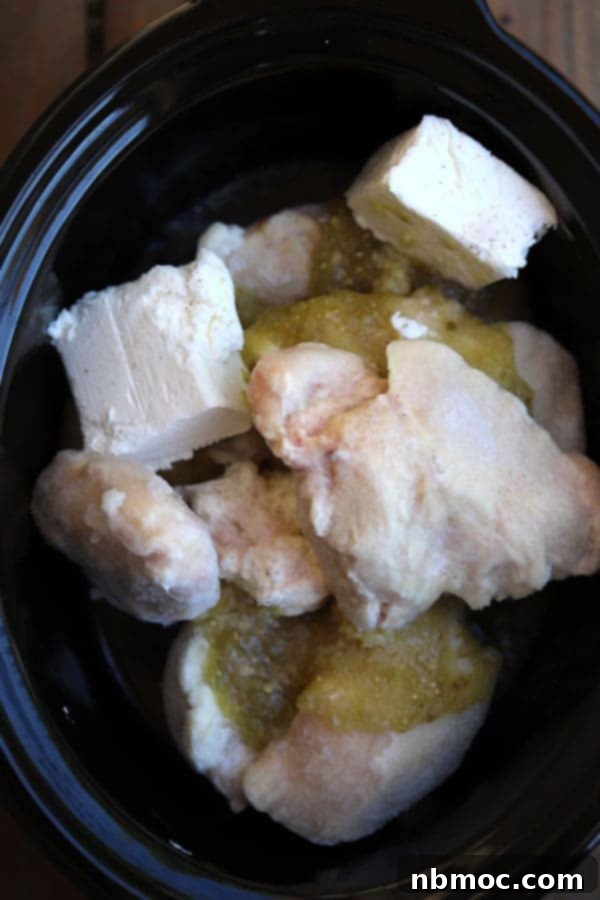 Crockpot full of ingredients to make salsa verde chicken, showcasing fresh chicken breasts, salsa verde, and cream cheese.