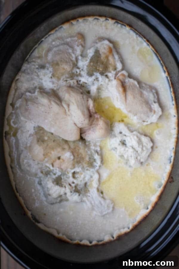 Salsa verde chicken cooking in a crockpot, showing the creamy green sauce bubbling around the chicken.