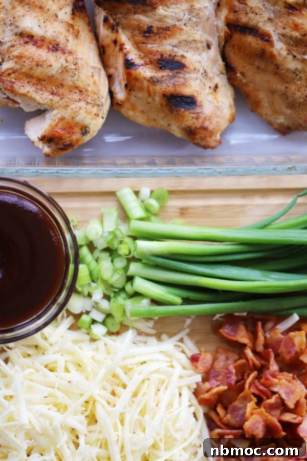 Grilled chicken for monterey chicken in a baking dish next to BBQ sauce, shredded cheese, bacon, and green onions.