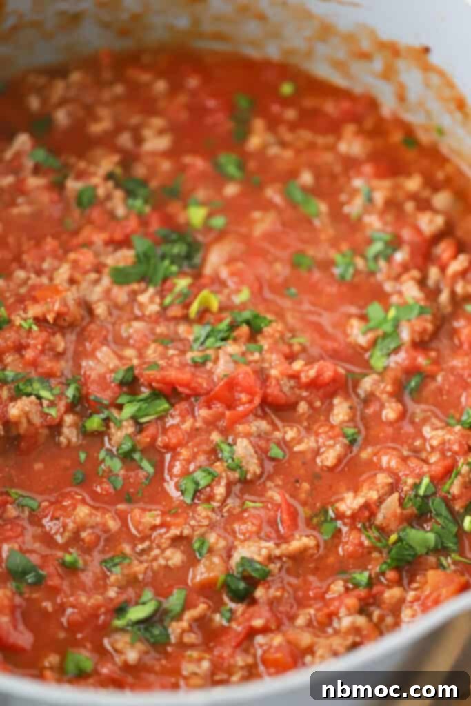 Rich Homestyle Meat Sauce 2 A large saucepan full of homemade meat sauce for spaghetti, topped with fresh green herbs.