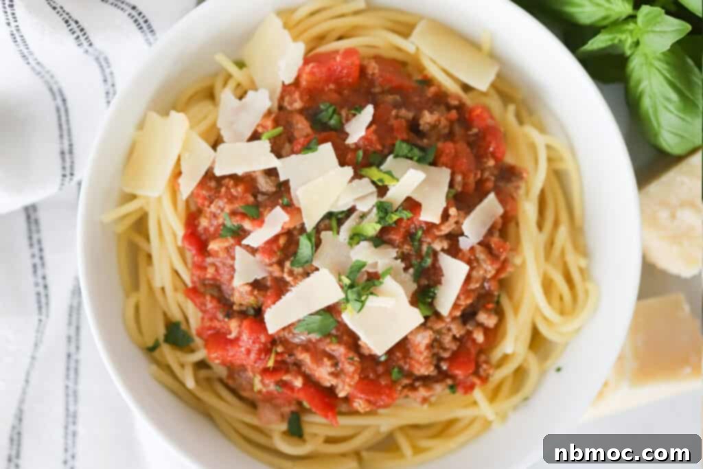Rich Homestyle Meat Sauce 3 A bowl of spaghetti topped with meat sauce, grated Parmesan cheese, and fresh herbs.