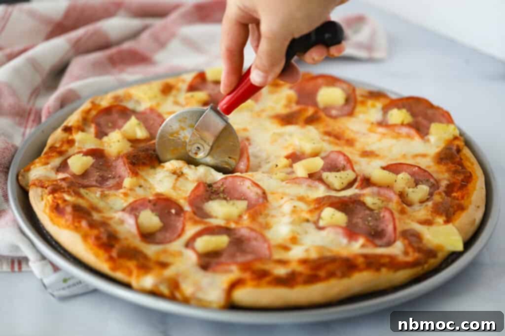 Best Hawaiian Pizza Recipe 3 A hand cutting a Hawaiian pizza recipe with the pizza cutter.