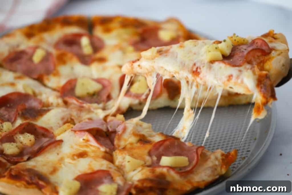 Best Hawaiian Pizza Recipe 6 A sliced Hawaii pizza on a baking sheet with a slice being removed by a spatula.