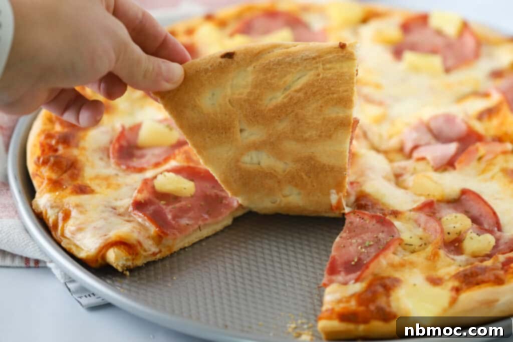 Best Hawaiian Pizza Recipe 7 A hand grabbing a slice of Hawaii pizza from a pizza tray.