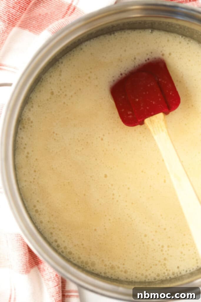 Velvety Buttermilk Syrup Perfection 5 Homemade buttermilk syrup in a pan being stirred with a spatula, showing its rich texture.