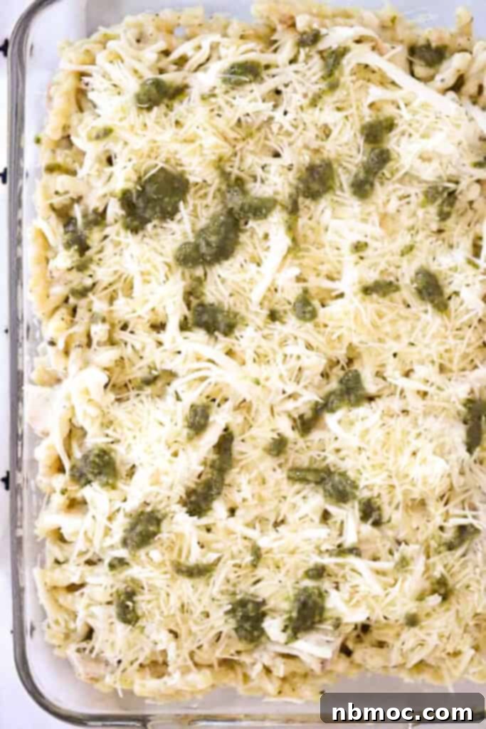 A baking dish layered with pasta, chicken, cheese and pesto ready to bake.