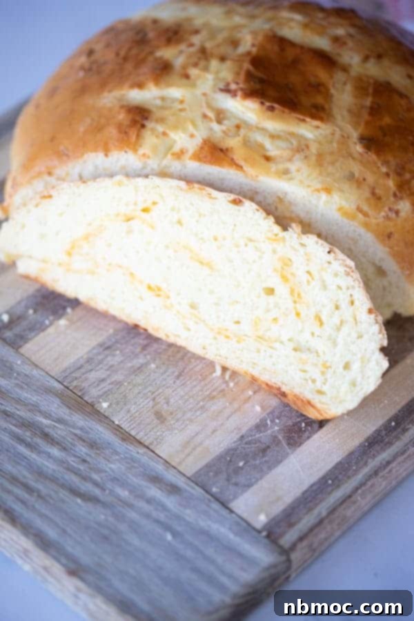 A cutting board with a loaf of homemade cheese bread being sliced.