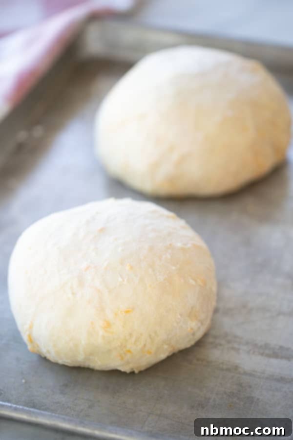 Two dough balls of cheddar bread on a cutting board.