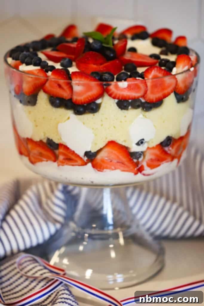 Beautifully layered berry trifle in a large glass dish, featuring star-shaped pound cake pieces, fresh strawberries, and blueberries, garnished with mint.
