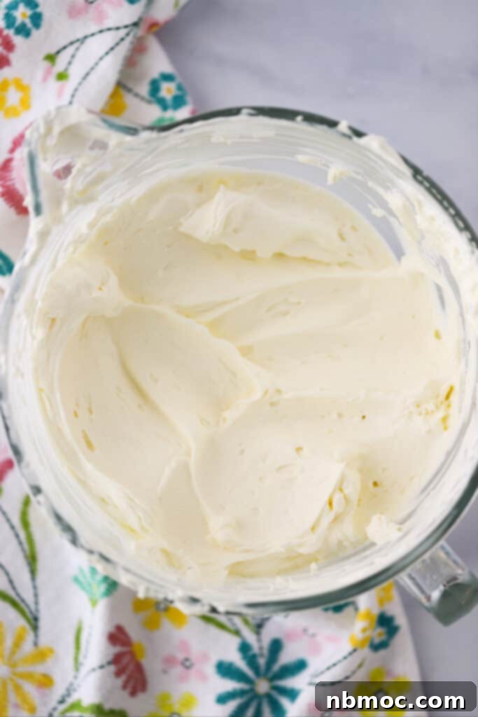A large glass bowl filled with the smooth, fluffy whipped cream and cream cheese mixture on a rustic wooden table, ready for trifle assembly.