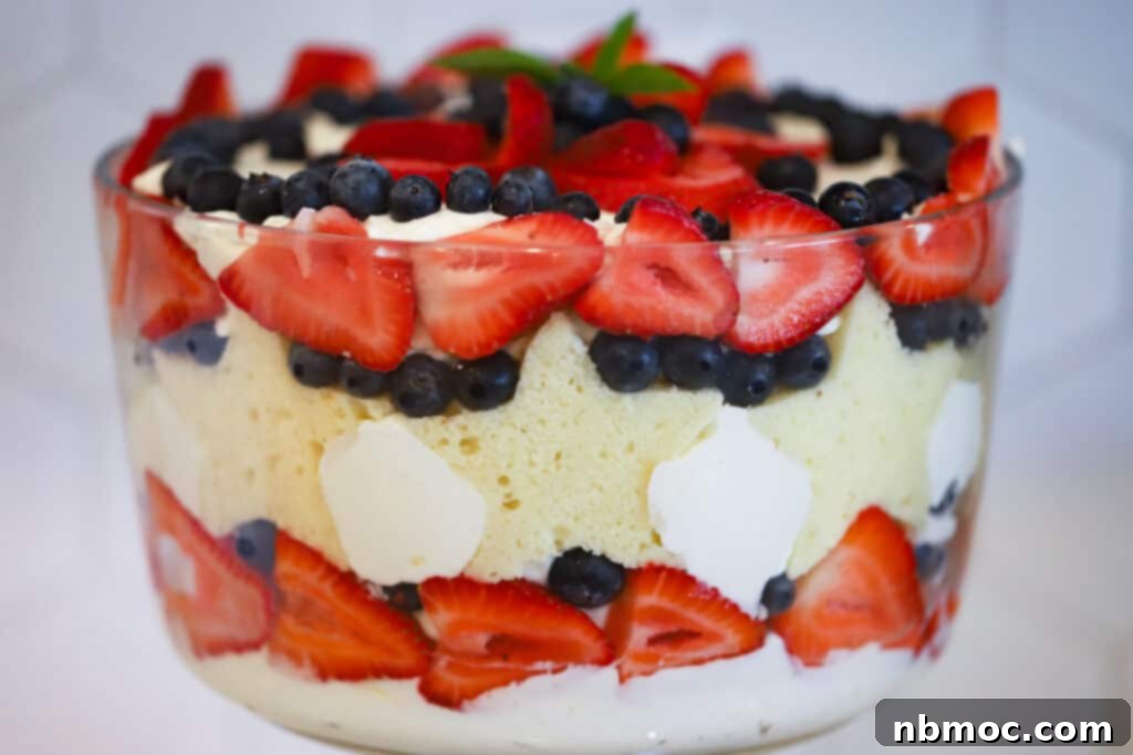 A stunning side view of a patriotic 4th of July Berry Trifle, showcasing layers of vibrant strawberries, blueberries, and pound cake, beautifully garnished with a sprig of fresh mint.