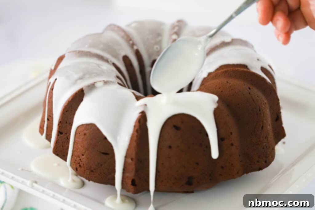 Decadent Chocolate Pound Cake 5 A glorious chocolate bundt cake sitting on a serving plate, with luscious chocolate pound cake icing being artfully poured over its top using a spoon, highlighting a cream cheese chocolate pound cake recipe.