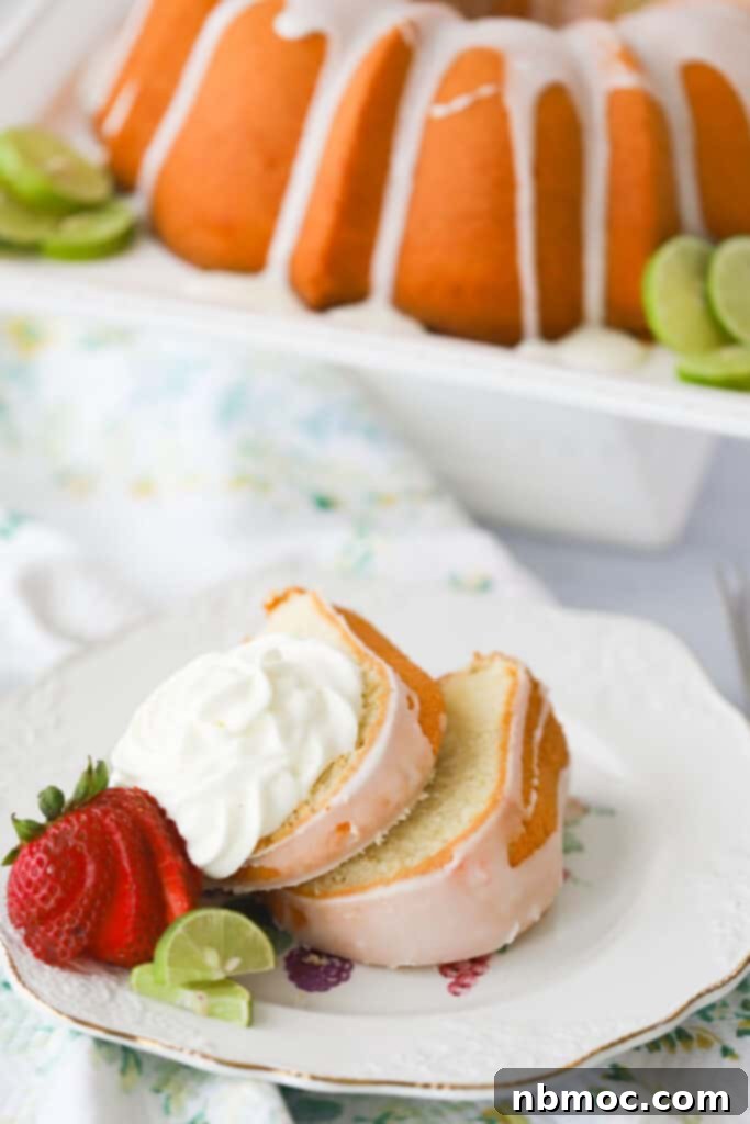 Florida Keys Pound Delight 3 A serving plate with glazed Key Lime Pound Cake, topped with whipped cream and fresh strawberries. A full pound cake is in the background on a cake stand.