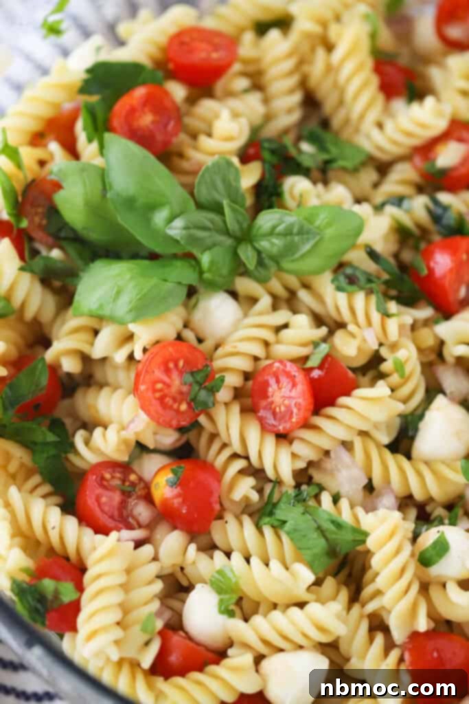 A close up of Caprese Pasta salad recipe, topped with fresh basil and cherry tomatoes.