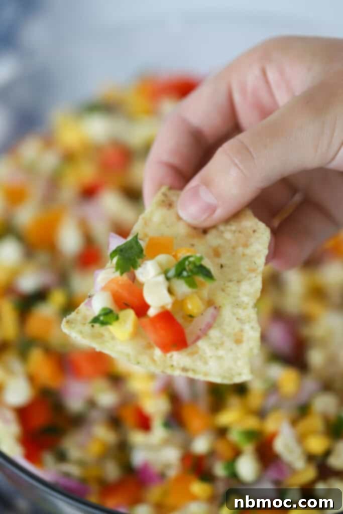 A hand holding a chip with our Easy Corn Salsa on it; corn appetizer; canned corn salsa recipe.