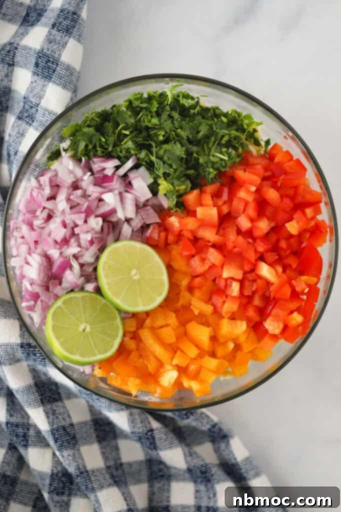A mixing bowl with chopped red onions, cilantro, bell peppers and a sliced lime ready to be mixed.