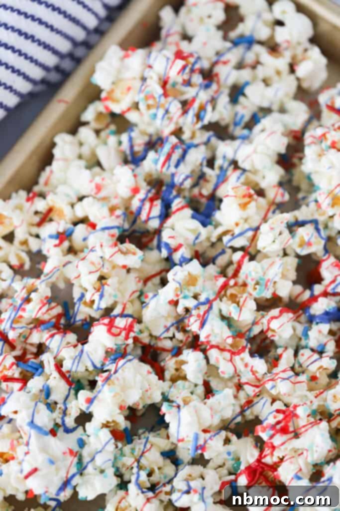 A baking tray that is covered in a layer of firecracker popcorn decorated with red, white and blue drizzle and candies.