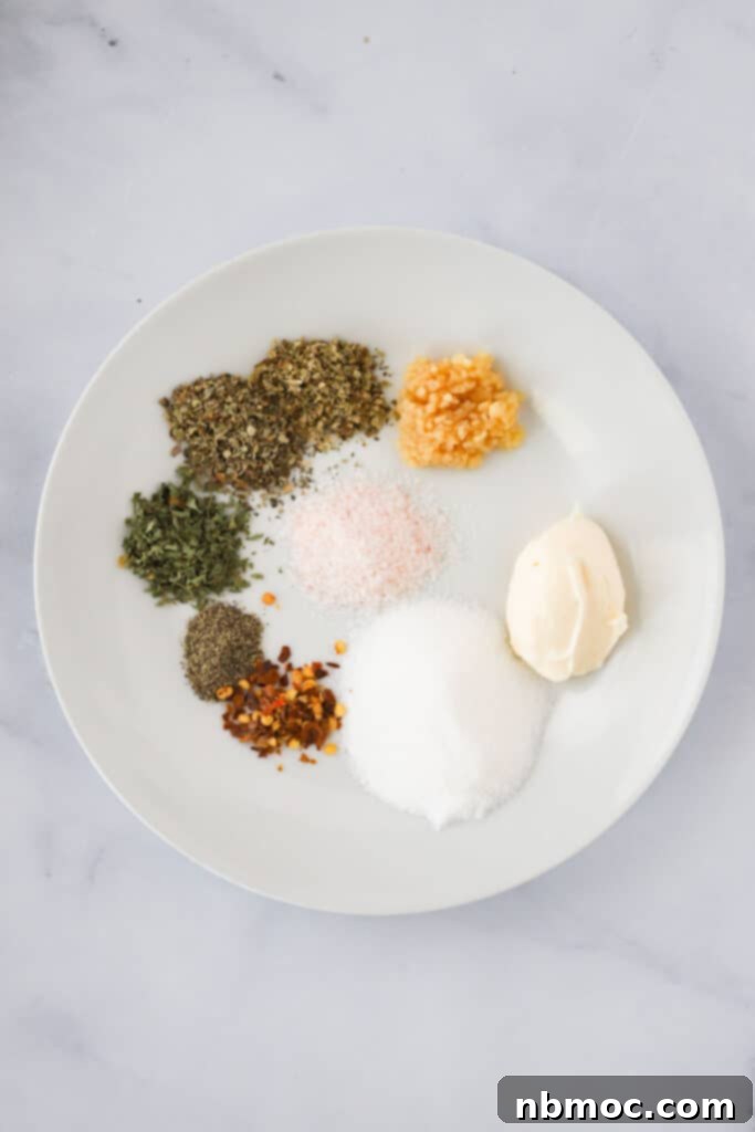 Zesty Italian Vinaigrette 3 A small white bowl showcasing the key ingredients for homemade salad dressing, including dried herbs, salt, sugar, and mayonnaise, laid out on a clean surface.