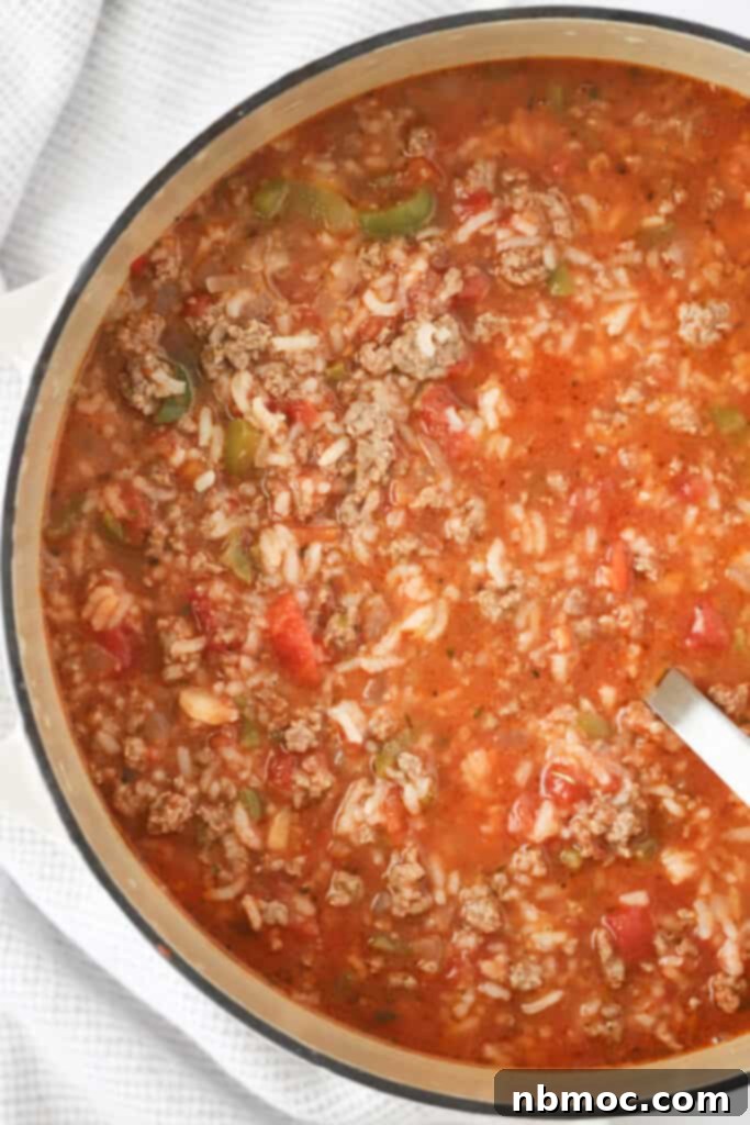 A large Dutch oven filled with hearty stuffed green pepper soup, featuring ground beef, rice, colorful vegetables, and a rich tomato-based broth, ready to be served.