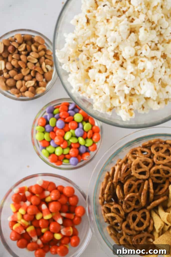 Small bowls full of ingredients to make this party mix snack, showcasing fresh popcorn, pretzels, Bugles, and peanuts.