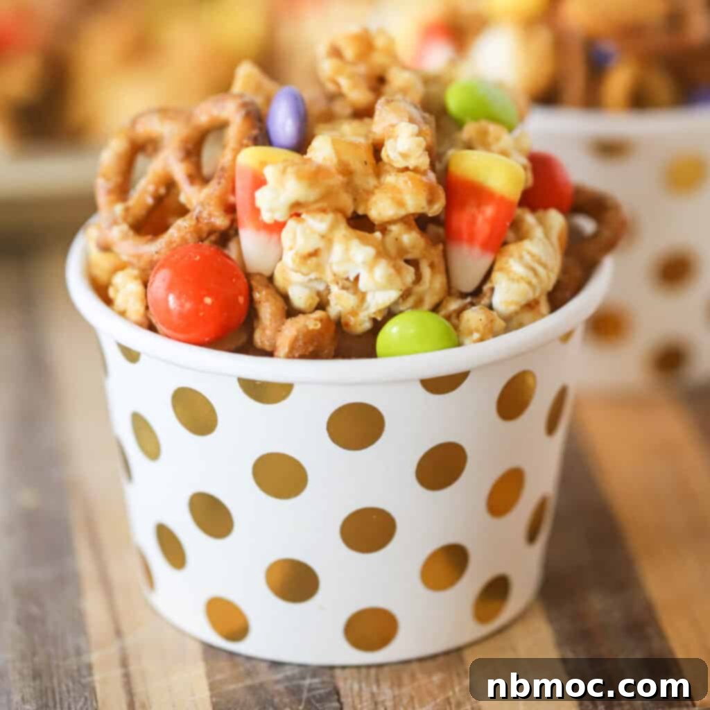 A small decorative cup filled with Halloween Chex mix made with pretzels, popcorn, and candy, highlighting its festive appeal.