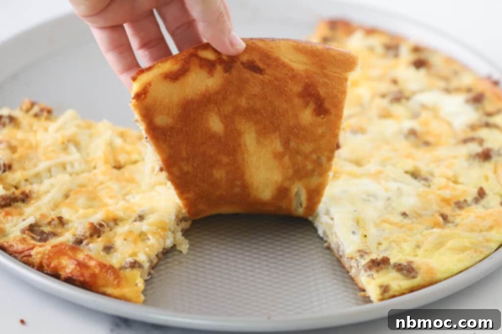 A hand reaching for a slice of warm Breakfast Pizza from a pan, showing the golden crust and generous toppings of sausage, hash browns, and eggs.