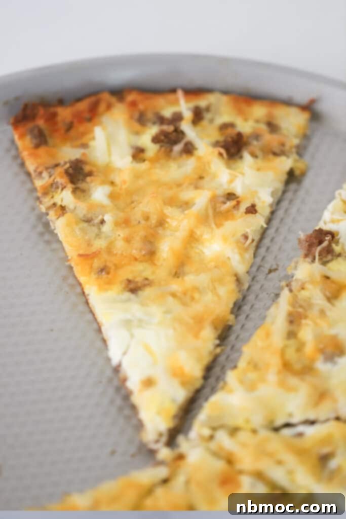 A close-up shot of a slice of breakfast pizza, featuring a rich egg and cheese topping with visible bits of sausage and hash browns, resting on a pizza pan.
