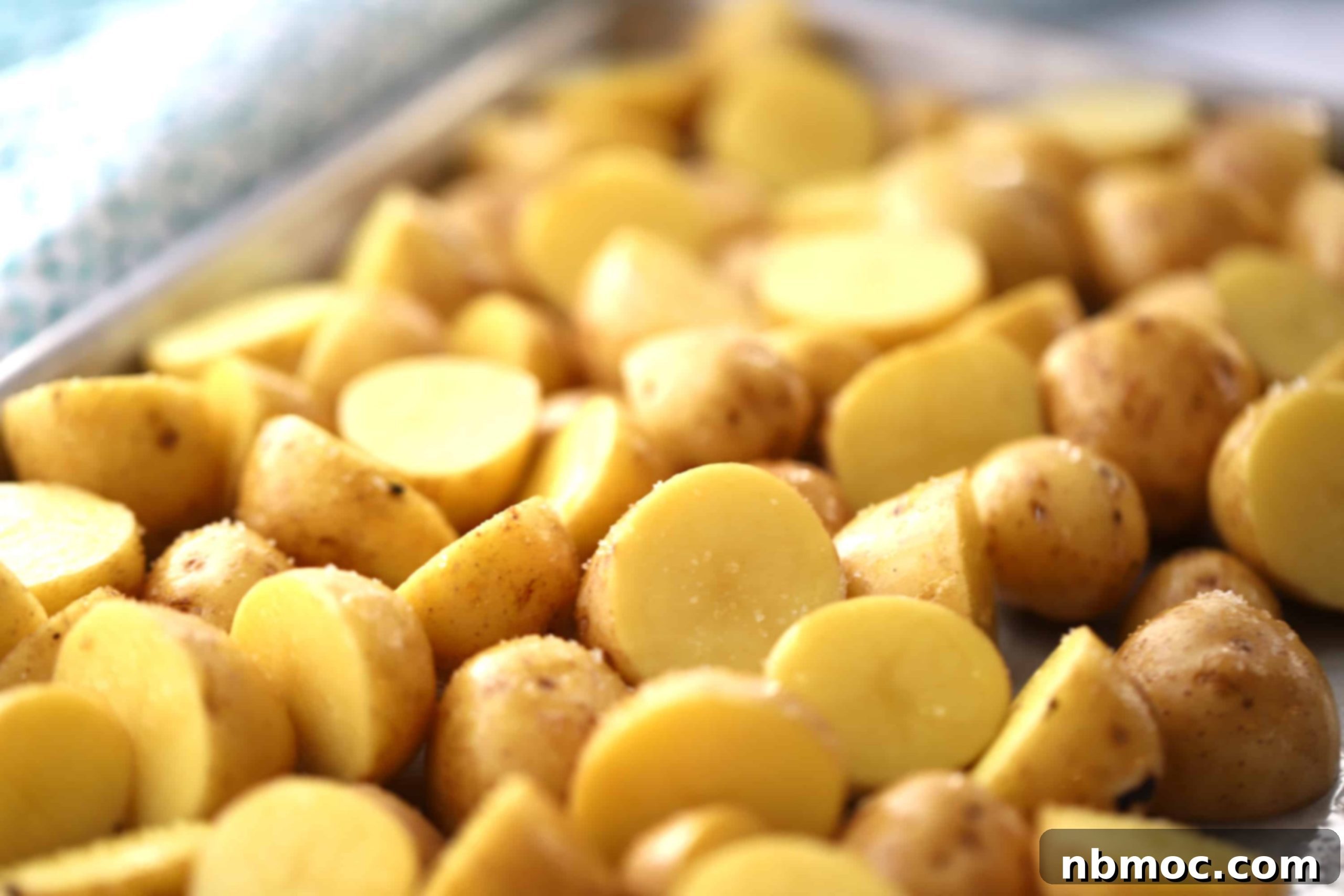Small potatoes, uniformly cut in half and spread out in a single layer on a baking sheet, ready for roasting.