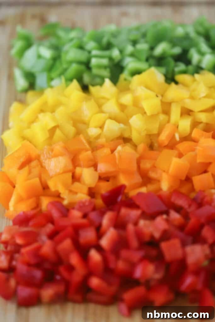 Diced green, yellow, orange, and red bell peppers arranged neatly on a cutting board, prepared for freezing.