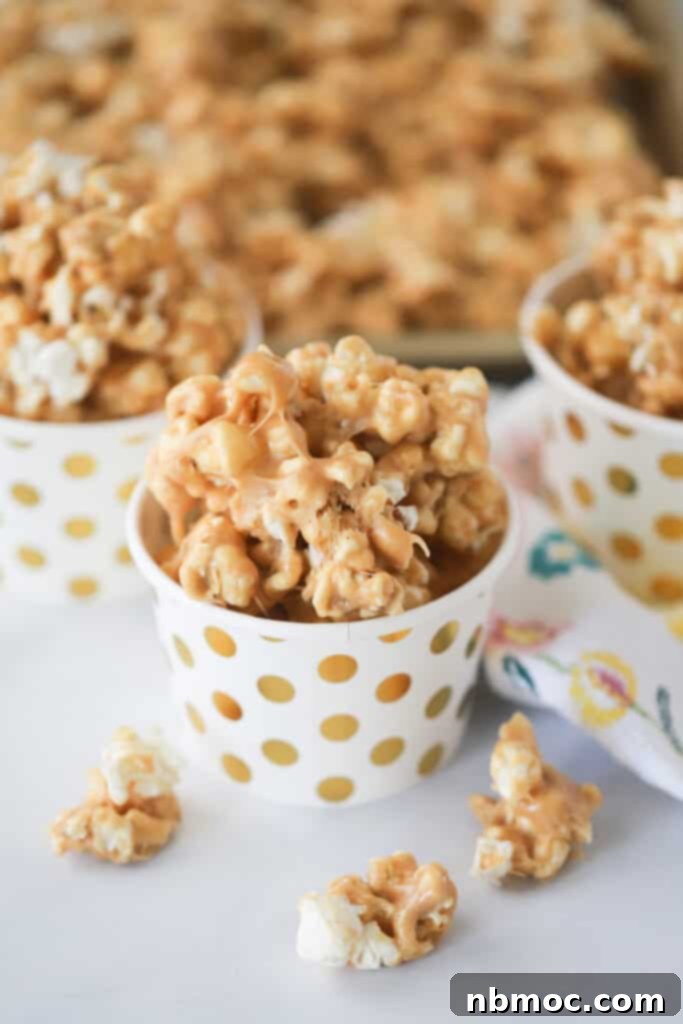 Small white cups with gold dots filled with Peanut Butter Popcorn, a simple popcorn dessert made with peanut butter, caramel, and marshmallows.