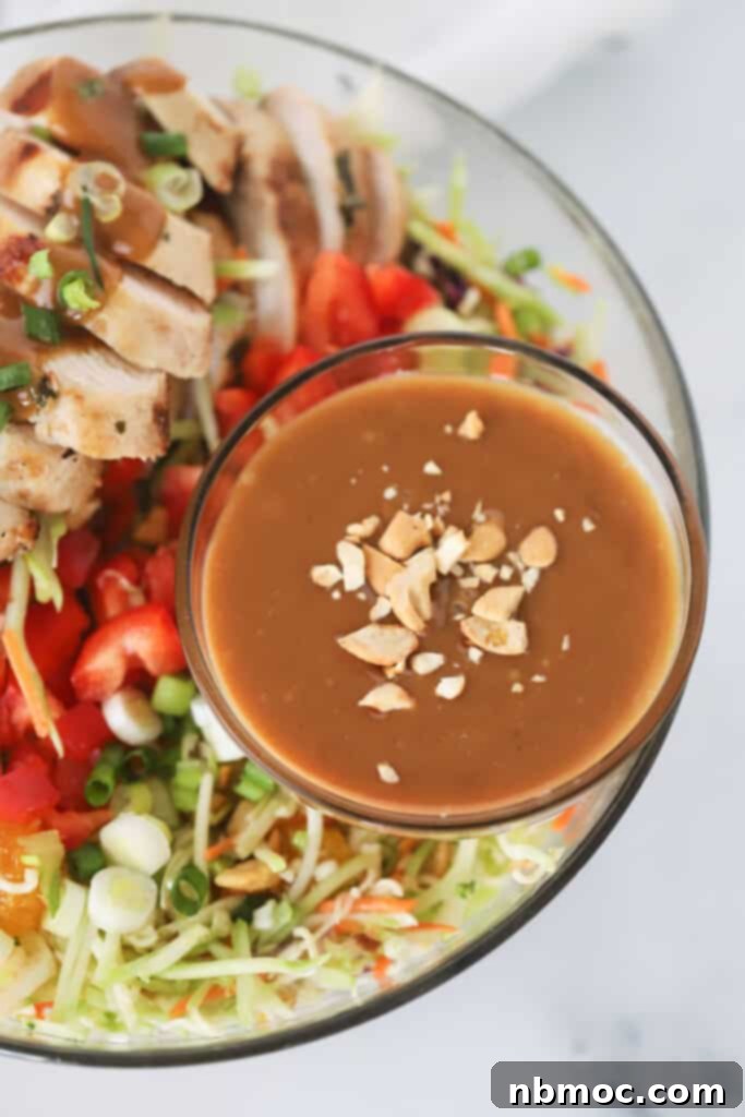 A bowl of chicken thai salad made with fresh veggies, sliced chicken breast, and a ramekin full of peanut sauce. chopped salad with chicken. Chicken thai salad.