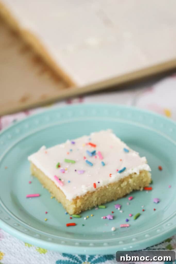Classic White Texas Sheet Cake 2 A slice of white Texas sheet cake on a plate, topped with colorful sprinkles and white frosting.