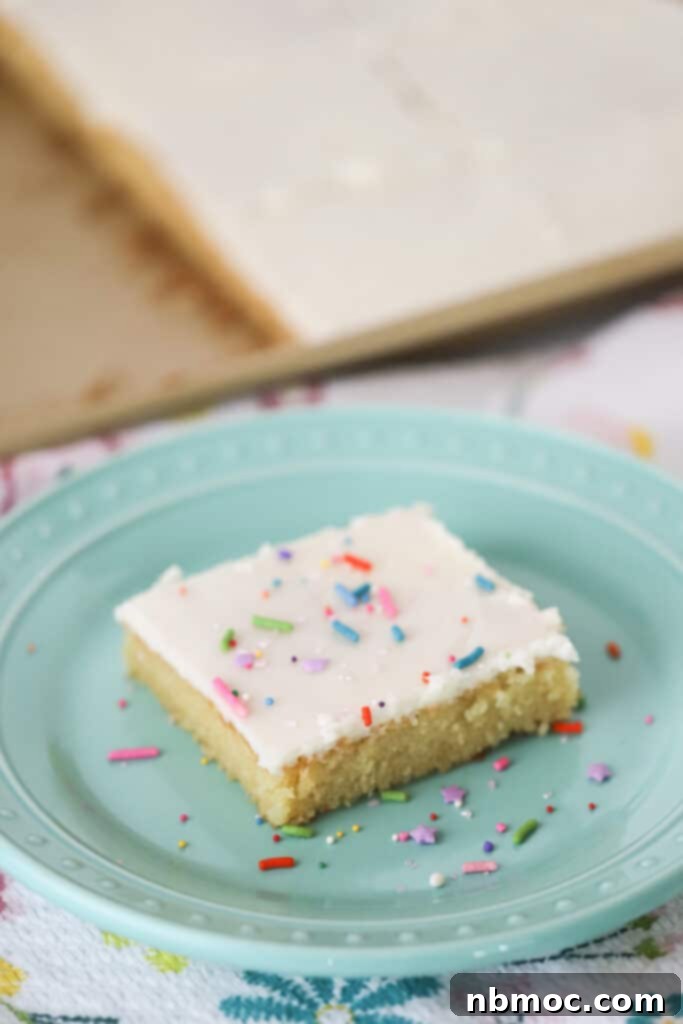 Classic White Texas Sheet Cake 4 A decorative blue plate with a slice of Texas White Sheet Cake topped with frosting and rainbow sprinkles.
