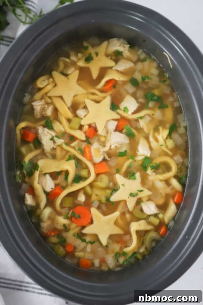 Slow cooker chicken noodle soup inside the slow cooker with star shaped noodles.