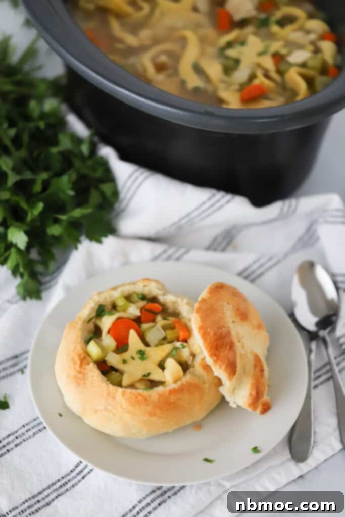A white serving plate with a bread bowl full of slow cooker chicken noodle soup.