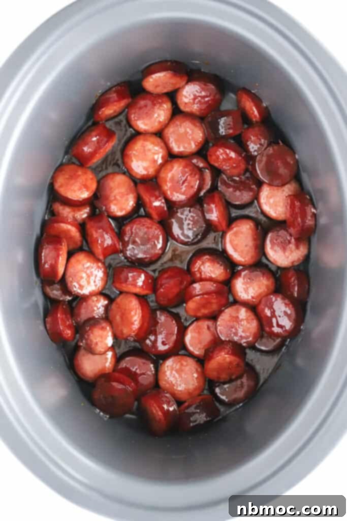 A slow cooker filled with glistening, sliced candied kielbasa ready to be served.