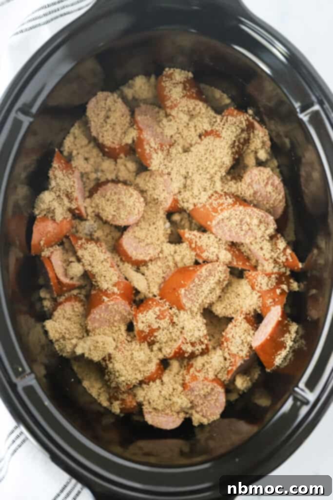 Sliced kielbasa in a slow cooker, generously covered with dark brown sugar before cooking.