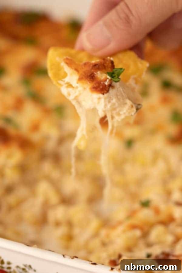 Vibrant Fiesta Corn Dip 3 A hand dipping a tortilla chip into a freshly baked Fiesta Corn Dip, showing the gooey cheese and corn mixture.