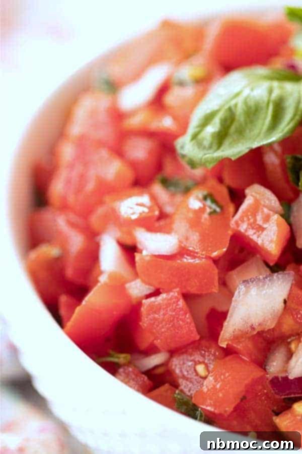 bruschetta tomatoes recipe in a white bowl topped with fresh basil.