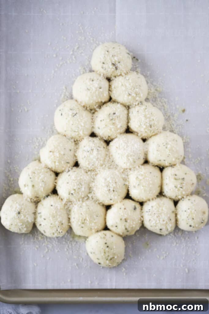 Garlic Butter Christmas Tree Rolls 3 Balls of dough arranged in the shape of a festive Christmas tree on a baking sheet, generously topped with grated Parmesan cheese and garlic salt before baking. These homemade garlic rolls are perfect for holidays.