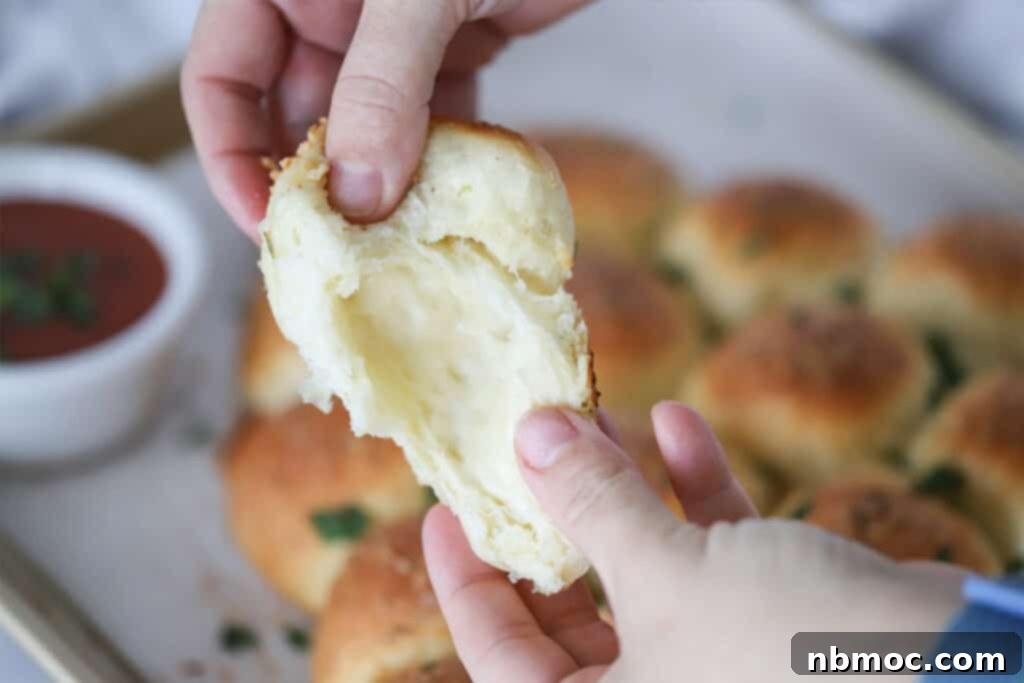 Garlic Butter Christmas Tree Rolls 4 Two hands pulling apart a warm, golden-brown pull-apart roll, revealing the melted, stretchy mozzarella cheese inside. This highlights the delicious cheese-stuffed aspect of the garlic rolls recipe.