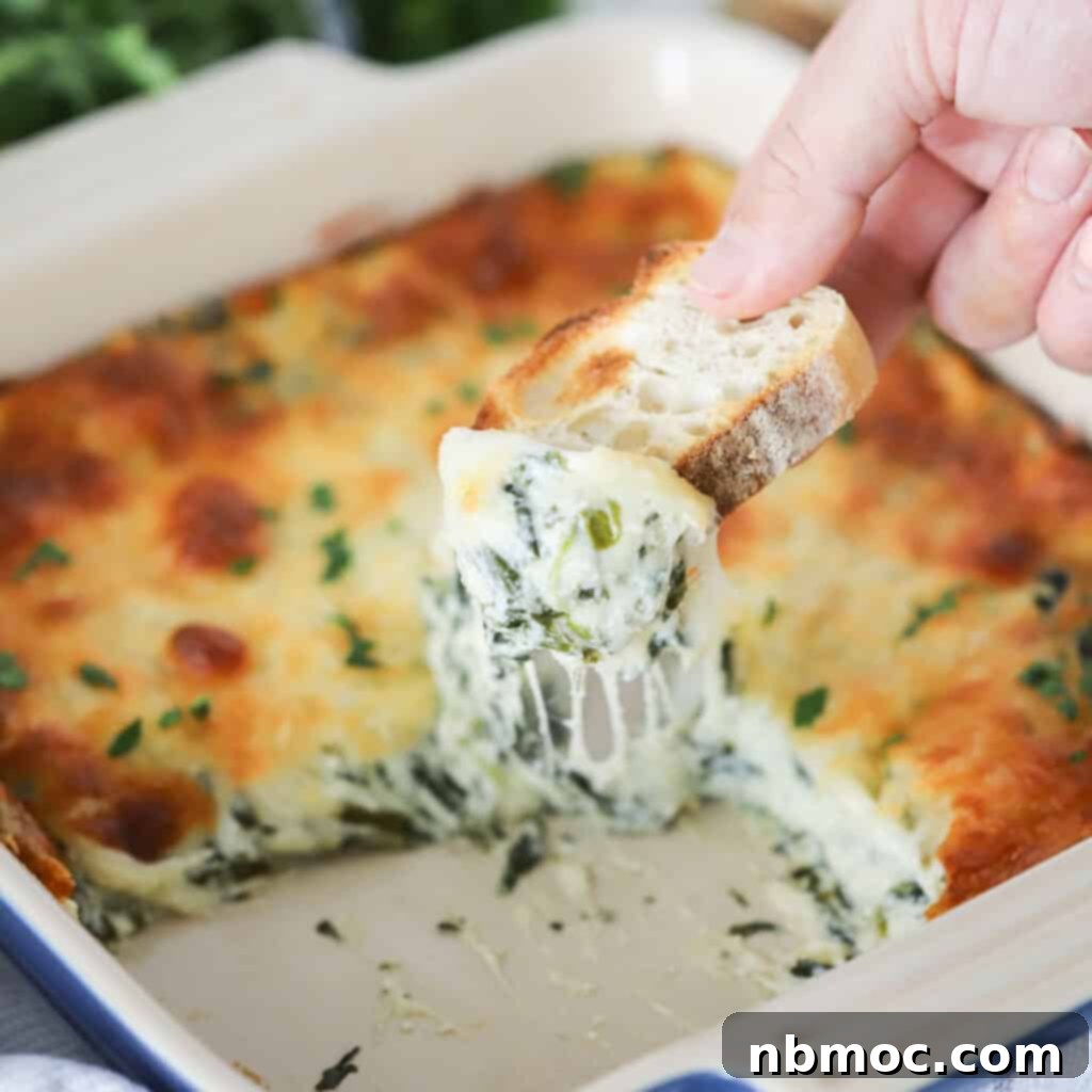 Creamy Spinach Delight 4 A hand holding a baguette slice that has been dipped into spinach dip, showcasing the creamy texture and inviting presentation.