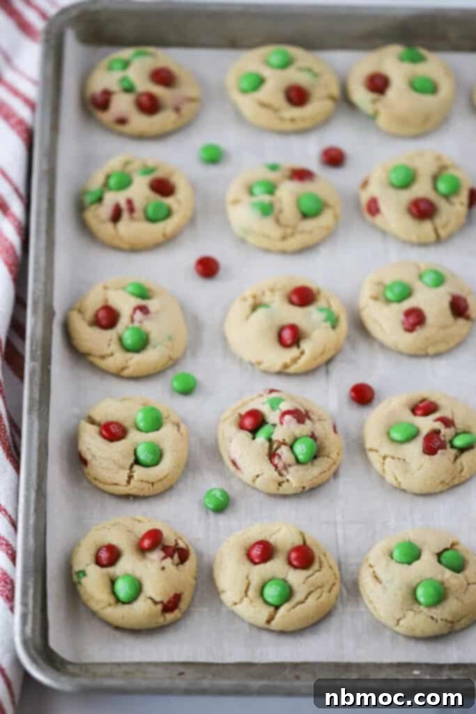 Close-up of a batch of freshly baked Christmas M&M cookies cooling on a wire rack, showcasing their vibrant red and green candies.