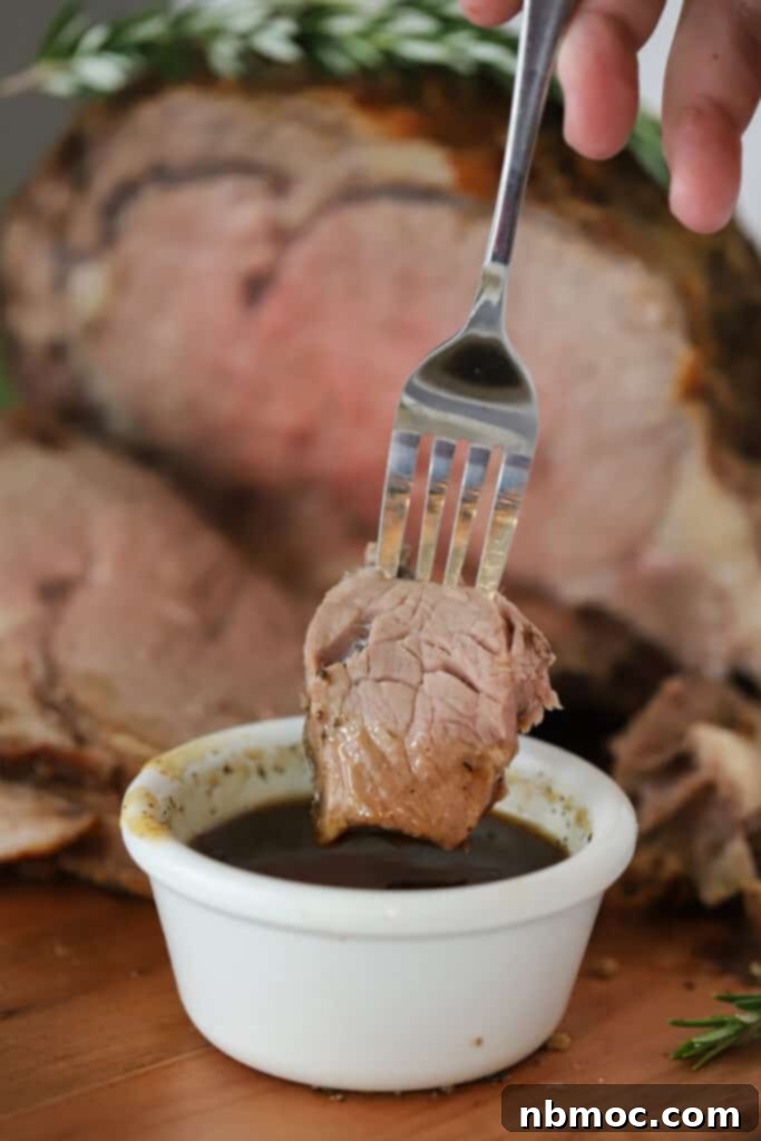 A fork holding a piece of perfectly cooked beef being dipped into a rich au jus, highlighting the tenderness and savory flavor.