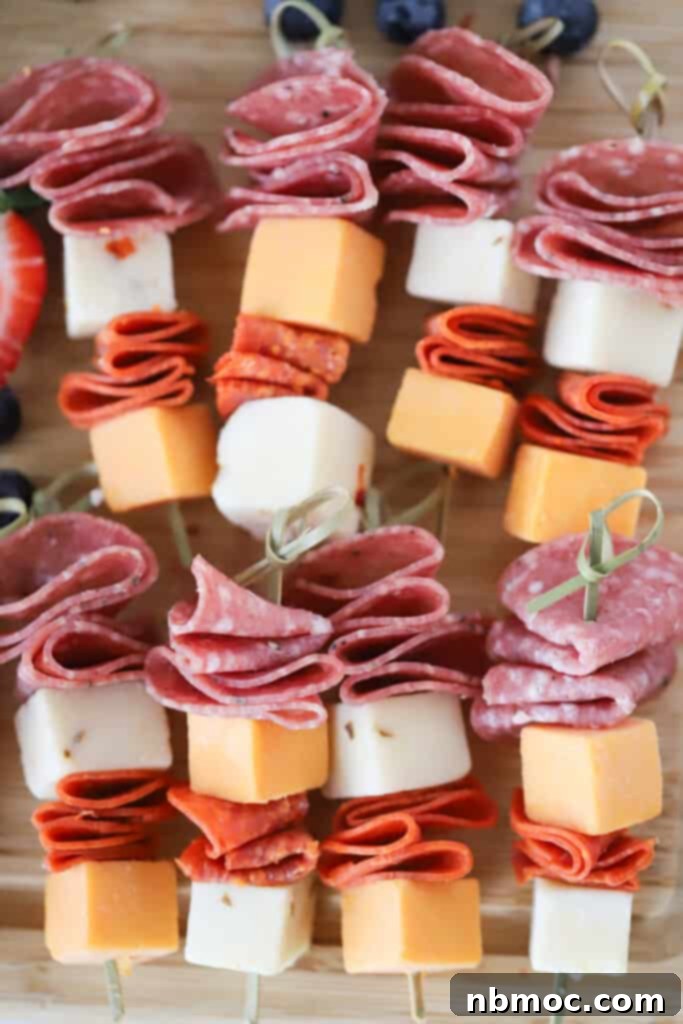 Preparing skewers with sliced salami, pepperoni, and cheese cubes for individual charcuterie cup appetizers.