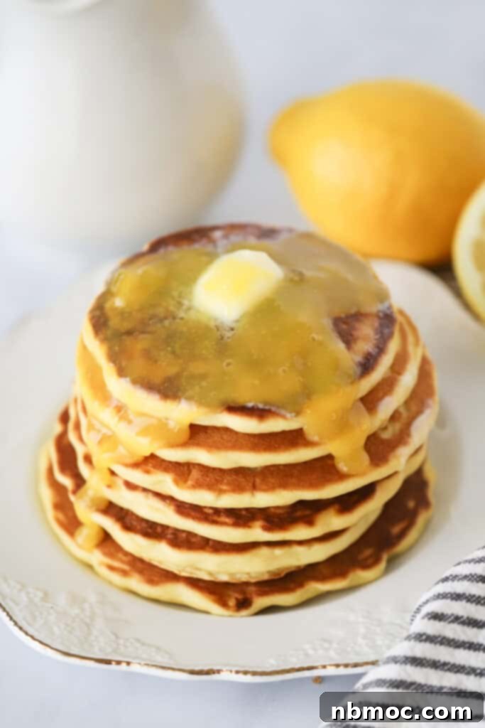 A stack of lemon ricotta cheese pancakes on a white plate with butter melting over the top.