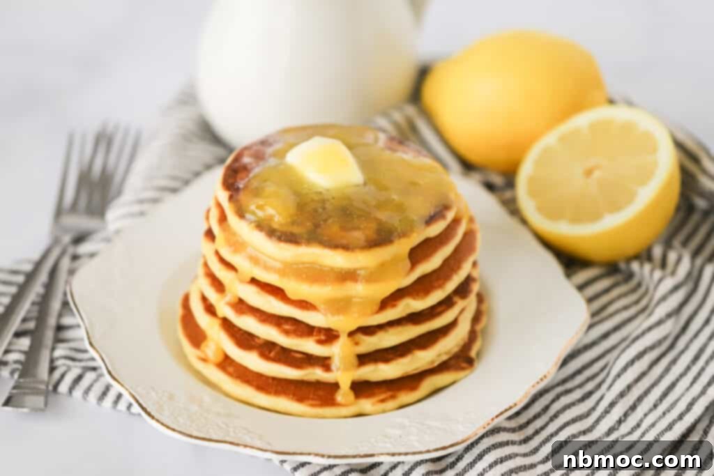 A stack of Lemon Ricotta Pancakes topped with melted butter on a white serving plate. 